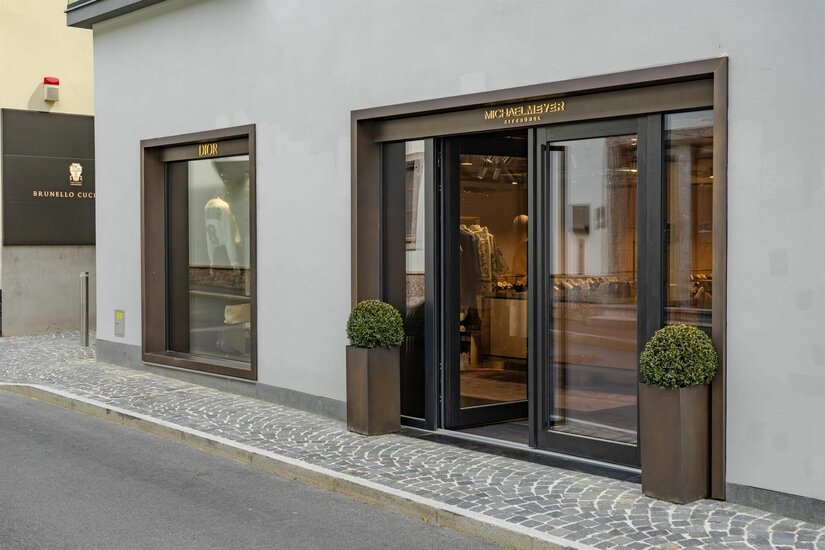 Modegeschäft Michael Meyer Eingangsbereich eines Modegeschäfts mit Glasfront und dunklen Metallrahmen an einer gepflasterten Straße.