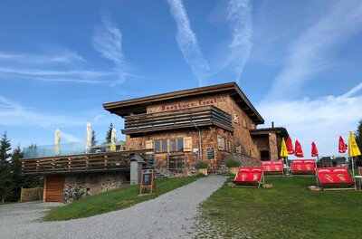 Berghaus Tirol mit Holzfassade, Terrasse und Liegestühlen unter blauem Himmel.