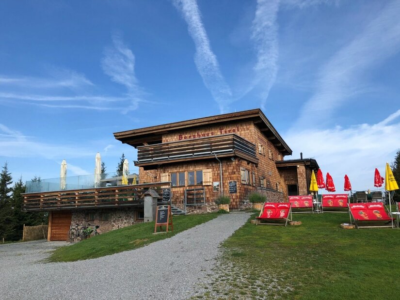 Berghaus Tirol Berghaus Tirol mit Holzfassade, Terrasse und Liegestühlen unter blauem Himmel.