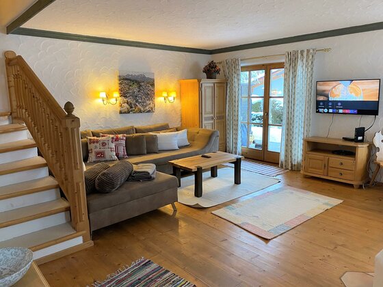 Wohnbereich Haus Staudach Wohnzimmer mit Ecksofa, Holztisch, TV und einer Holztreppe in einem alpinen Ferienhaus.