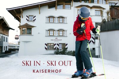Ein Skifahrer steht auf Schnee vor dem Hotel Kaiserhof. Im Hintergrund sind eine traditionelle Alpenarchitektur und der Schriftzug „SKI IN - SKI OUT“ zu sehen.