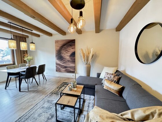 IMG_5265 Large Ein modernes Wohnzimmer mit einer gemütlichen Couch, einem Kaffeetisch und einem Esstisch. Große Fenster und stilvolle Dekoration schaffen eine einladende Atmosphäre.