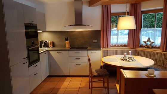 Moderne Einbauküche mit hellen Fronten und angrenzender hölzerner Essecke mit Rundtisch.