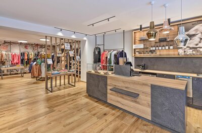 Innenansicht eines modernen Bekleidungsgeschäfts mit Holztheke und Kleiderstangen.