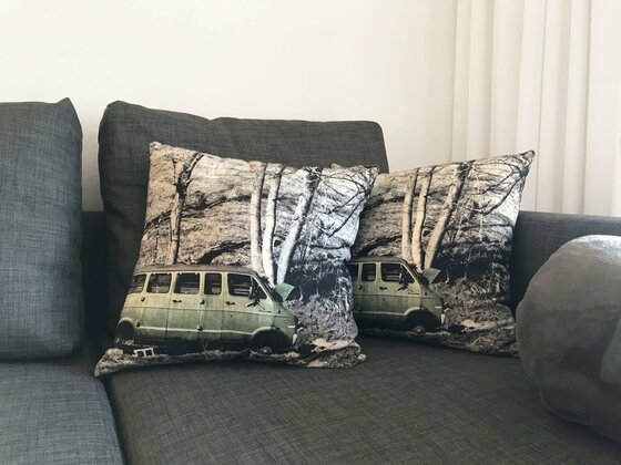 Apartment Hahnenkamm Dekoration Zwei Dekokissen mit einem Van-Motiv auf einem grauen Sofa.