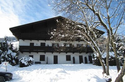 Mehrstöckiges weißes Gebäude mit Holzbalkonen in einer verschneiten Winterlandschaft unter blauem Himmel.