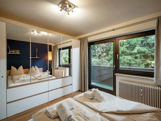 Modernes Schlafzimmer mit Doppelbett, großem Spiegelschrank und Balkonzugang.