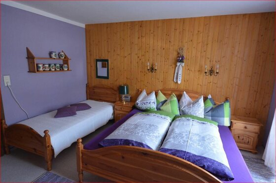 Gästezimmer im Haus Schneerose Schlafzimmer mit einem Doppelbett und einem Einzelbett aus Holz vor einer holzgetäfelten Wand.