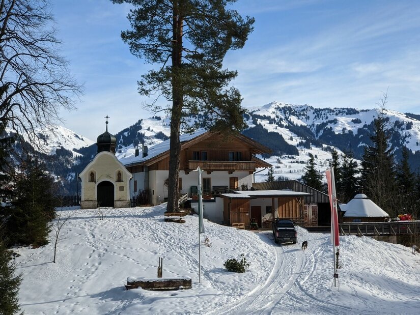 Einsiedelei im Winter Kleine Kapelle und ein alpines Gasthaus in einer verschneiten Berglandschaft mit Nadelbäumen.
