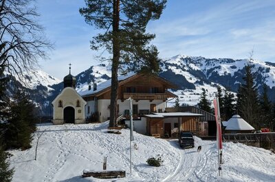 Einsiedelei im Winter Kleine Kapelle und ein alpines Gasthaus in einer verschneiten Berglandschaft mit Nadelbäumen.
