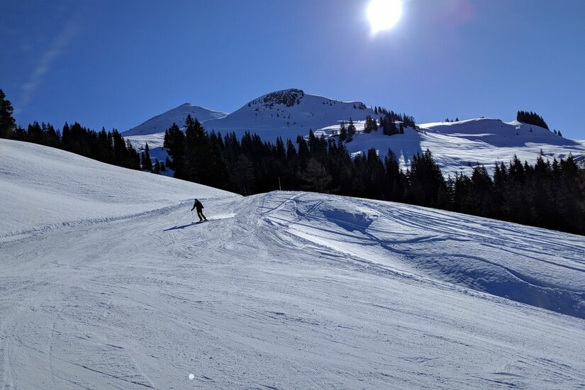 Skifahrer auf Skipiste am Schwarzkogel Ein Skifahrer auf einer präparierten Piste vor verschneiten Berggipfeln und blauem Himmel bei Sonnenschein.