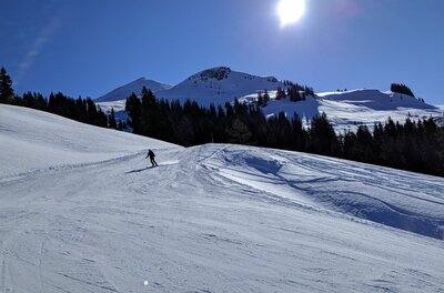 Skifahrer auf Skipiste am Schwarzkogel Ein Skifahrer auf einer präparierten Piste vor verschneiten Berggipfeln und blauem Himmel bei Sonnenschein.