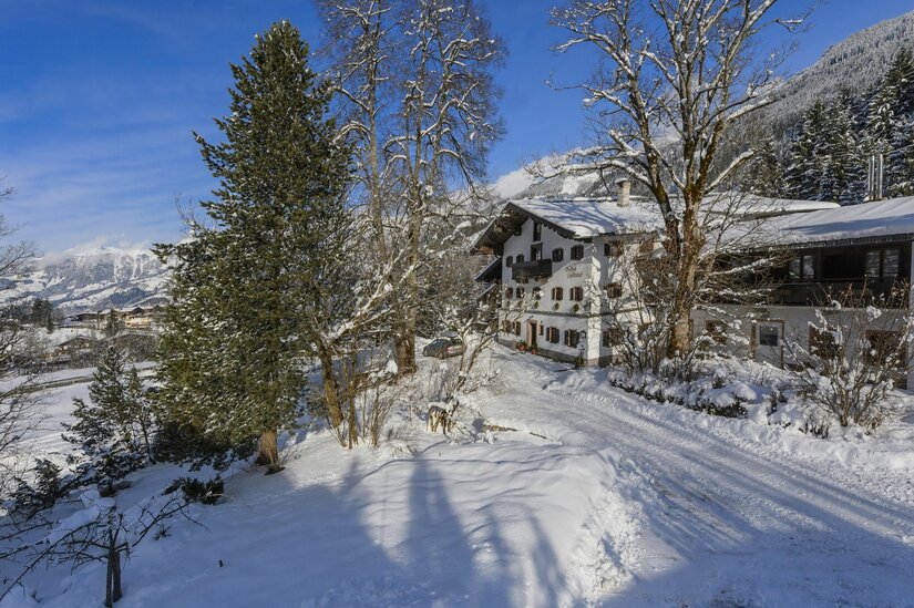 Landhotel Jodlbühel im Winter Verschneites Landhotel Jodlbühel mit schneebedeckten Bäumen und Bergen im Hintergrund.