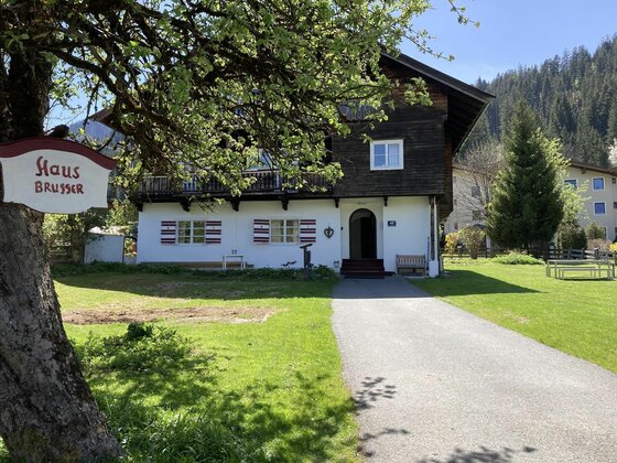 Zweistöckiges Haus mit weißer Fassade, dunklem Holzobergeschoss und Gartenweg.