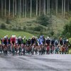 Eine Gruppe von Radfahrern beim Kitzbüheler Radmarathon fährt auf einer nassen Straße, umgeben von grünen Hügeln und Bäumen.