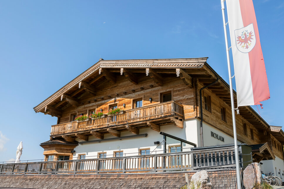 Ein traditionelles Holzhaus mit einem Balkon, geschmückt mit bunten Blumen, unter einem strahlend blauen Himmel.