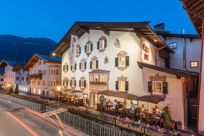 Beleuchteter Gasthof Eggerwirt in Kitzbühel bei Dämmerung mit Gästen auf der Außenterrasse.
