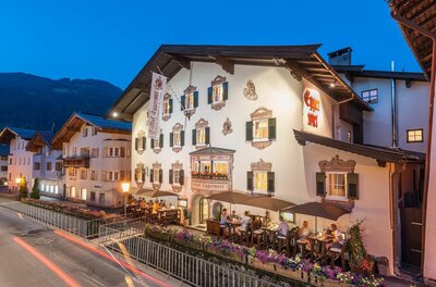 Beleuchteter Gasthof Eggerwirt in Kitzbühel bei Dämmerung mit Gästen auf der Außenterrasse.
