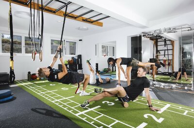 Training bei Sportscare Mehrere Personen trainieren in einem modernen Fitnessraum mit Kunstrasen, Seilen und Hanteln.