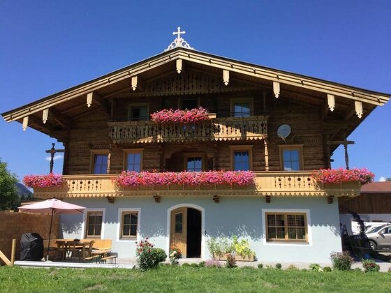 Fichterhof Kitzbühel im Sommer Dreistöckiges Holzhaus im alpinen Stil mit blumengeschmückten Balkonen vor blauem Himmel.