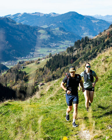 Die beiden Athleten tragen Rucksäcke und Sonnenbrillen, während sie sich durch die atemberaubende Berglandschaft bewegen.