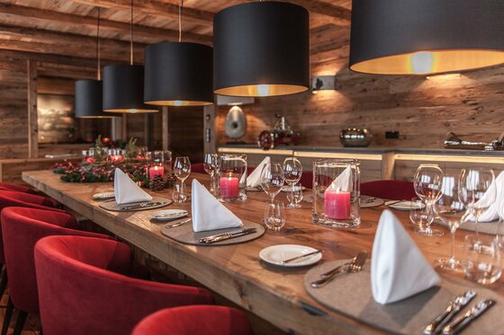 Gedeckter Holztisch mit roten Sesseln, weißen Servietten und schwarzen Hängelampen in einer Lodge.