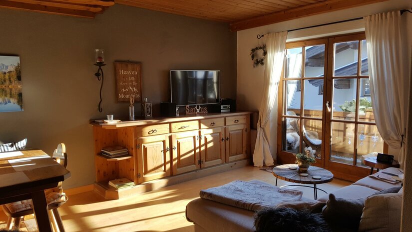 Wohnzimmer mit Holzmöbeln, Sofa, Fernseher und Balkonzugang.