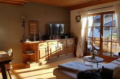 Wohnzimmer mit Holzmöbeln, Sofa, Fernseher und Balkonzugang.