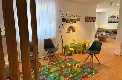Wartebereich einer Praxis mit Spielecke für Kinder, bunten Teppich und modernen Sitzmöbeln.
