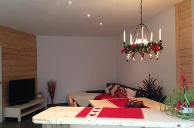 Wohnbereich mit Holztisch, Sofa, Fernseher und weihnachtlicher Dekoration.