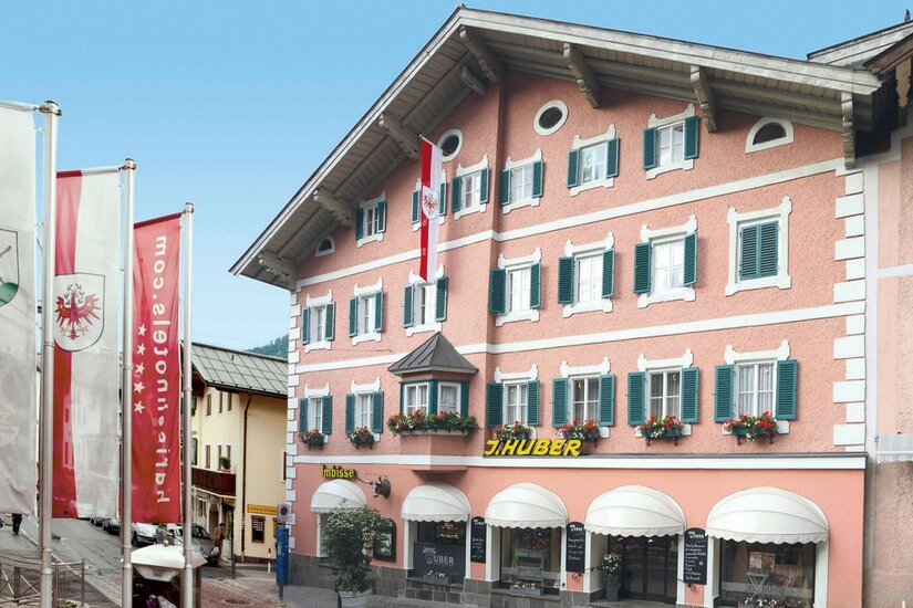 Metzgerei Huber Fassade Mehrstöckiges rosa Gebäude mit grünen Fensterläden und dem Schriftzug J. Huber.