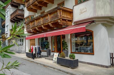 Eingangsbereich eines Bekleidungsgeschäfts mit roter Markise und Holzbalkon darüber.