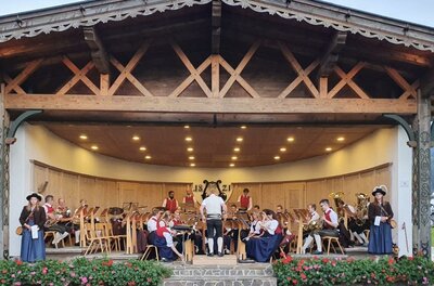 Eine festliche Veranstaltung mit einer Musikgruppe auf einer Bühne. Die Musiker tragen traditionelle Kleidung und umgeben sich mit Stühlen und Blumen.