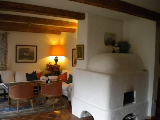Wohnzimmer Ferienhaus Giggling 3 Wohnzimmer mit weißem Kachelofen, Sitzgruppe und Holzbalkendecke.