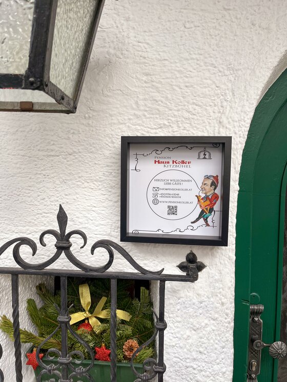 Eingang Pension Haus Koller Ein gerahmtes Hinweisschild der Pension Haus Koller an einer weißen Hauswand neben einer grünen Tür.