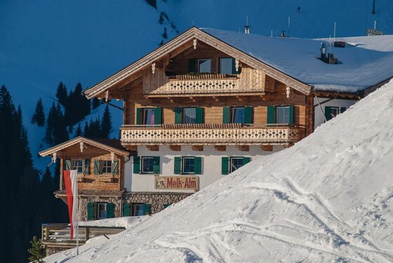 Berggasthof Melkalm im Winter Mehrstöckiger Berggasthof aus Holz und Stein in einer verschneiten Gebirgslandschaft.