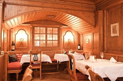 Rustikale Gaststube mit Holzvertäfelung, eingedeckten Tischen und gepolsterten Eckbänken.