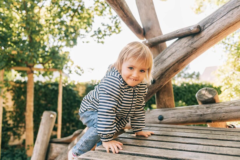 Kind auf Holzspielplatz Ein Kleinkind klettert auf einem Holzspielgerät im Freien.