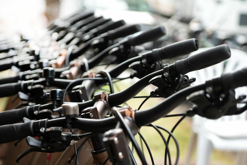 Nahaufnahme einer Reihe von Fahrradlenkern mit schwarzen Griffen und Klingeln bei einem Verleih.