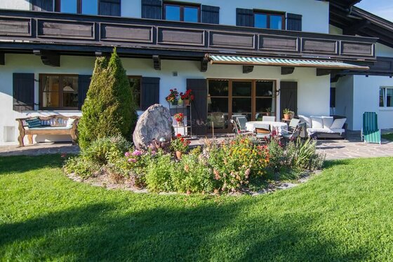 Terrasse eines Landhauses mit Gartenmöbeln, Blumenbeet und Rasenfläche.