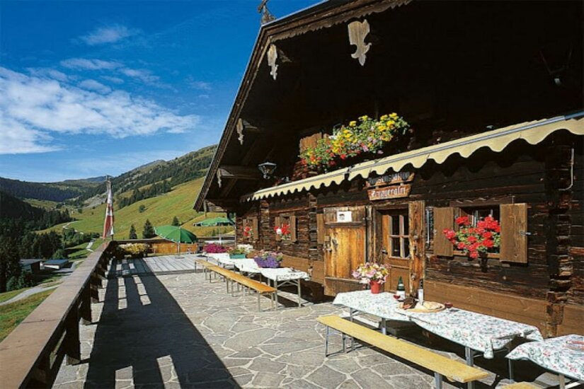 Terrasse der Bruggeralm Sonnenterrasse einer hölzernen Almhütte mit Sitzbänken und Blick auf grüne Berghänge.