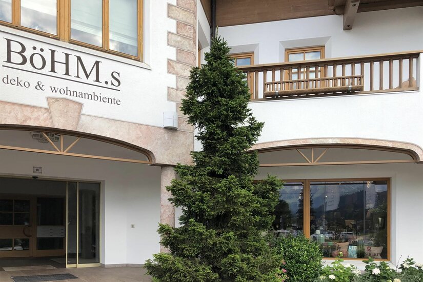 Eingangsbereich des Geschäfts Böhm.s mit Nadelbaum und Holzfassade.