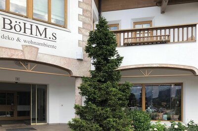 Eingangsbereich des Geschäfts Böhm.s mit Nadelbaum und Holzfassade.