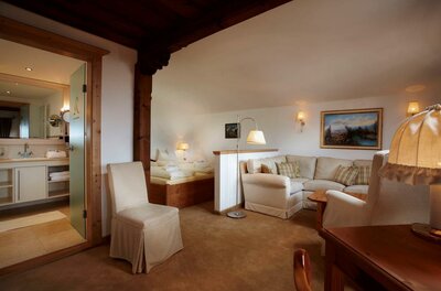 Wohnbereich in Rosi's Sonnbergstuben Wohn- und Schlafbereich eines Hotelzimmers mit hellem Sofa, Holzbett und angrenzendem Badezimmer.