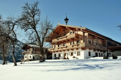 Alpiner Bauernhof aus Holz und Stein in einer verschneiten Winterlandschaft unter blauem Himmel.