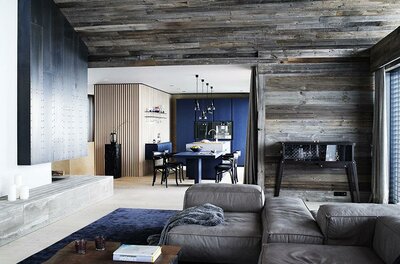 Moderner alpiner Wohnbereich Moderner Wohnraum mit Altholzwänden, grauem Sofa und blauer Küche im Hintergrund.