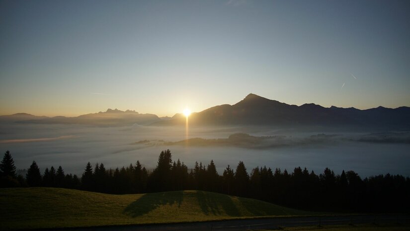 Bergausblick ostwärts am Wandhof Sonnenaufgang über einer Bergkette mit Nebel im Tal und Nadelwald im Vordergrund.