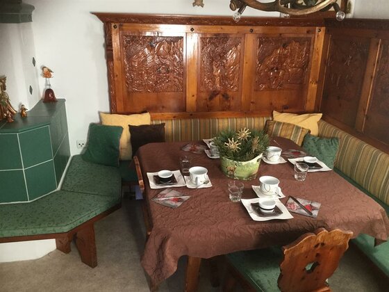 Gedeckter Holztisch mit Eckbank, Kissen und geschnitzter Wandverkleidung in einer rustikalen Stube.