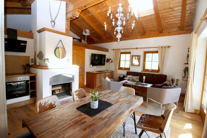 Rustikaler Wohn- und Essbereich mit Holztisch, Kamin, Sofa und sichtbarem Dachstuhl.