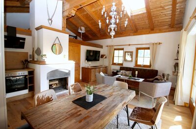 Rustikaler Wohn- und Essbereich mit Holztisch, Kamin, Sofa und sichtbarem Dachstuhl.